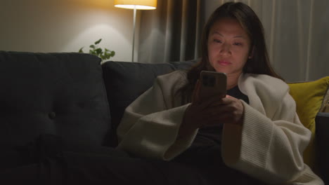 Woman-Spending-Evening-At-Home-Sitting-On-Sofa-With-Mobile-Phone-Scrolling-Through-Internet-Or-Social-Media-11